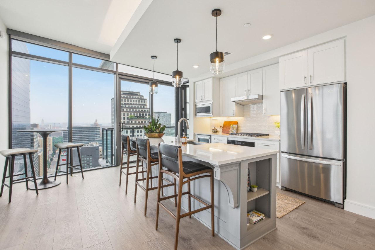 100-web-or-mls-colorado st model a5 classic-009 Kitchen with pendant lighting, bar-top with three chairs, white stone counters, stainless steel appliances, hardwood floors, and floor-to-ceiling windows