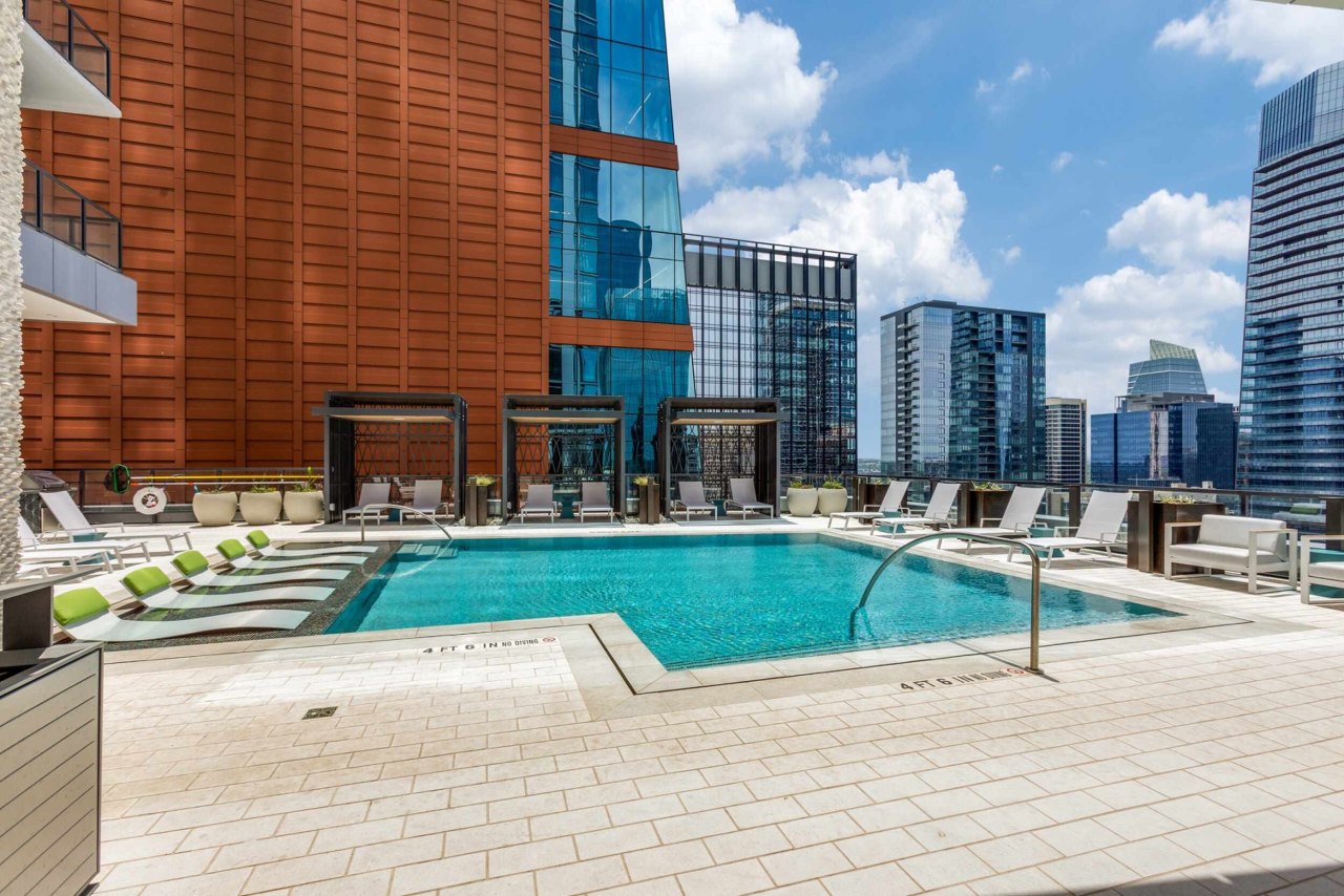 415-colorado-street-austin-tx-78701-high-res-81 -1- Luxury rooftop pool overlooking tall city buildings. Resort-style lounge chairs in and outside the water, cabanas surrounding the pool.